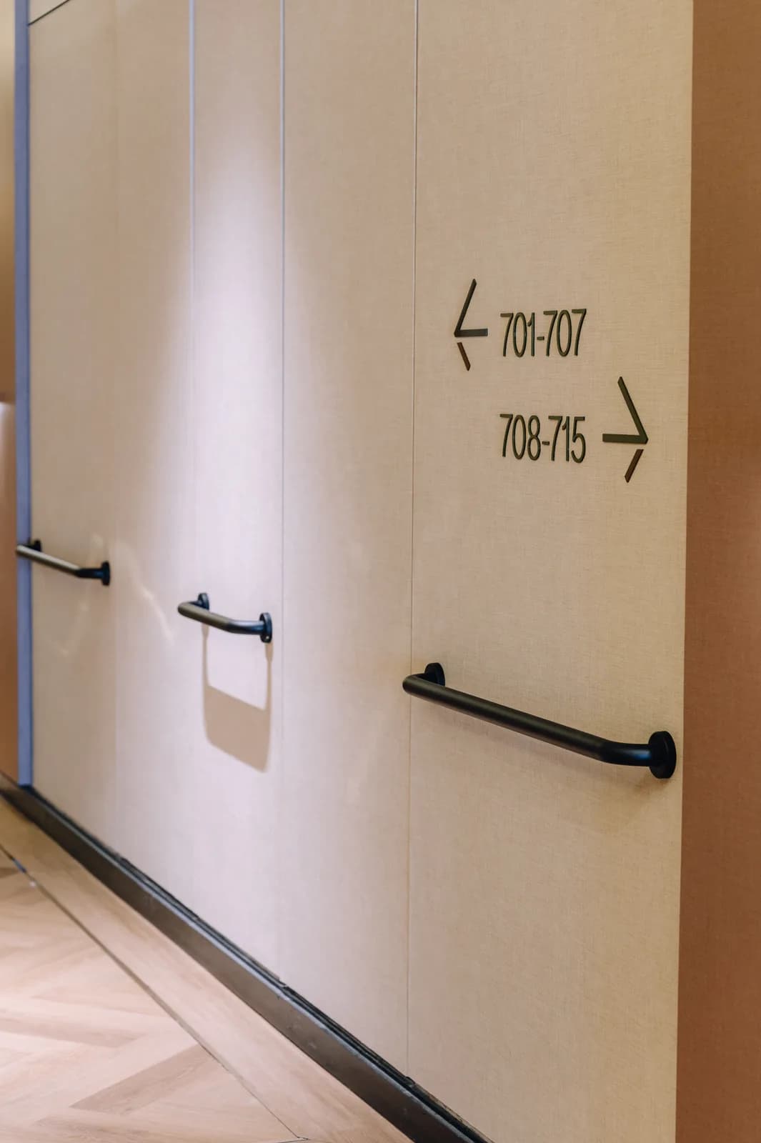 A corridor on an Assisted Living floor at Care Collective, with grab rails along the wall and room number signs