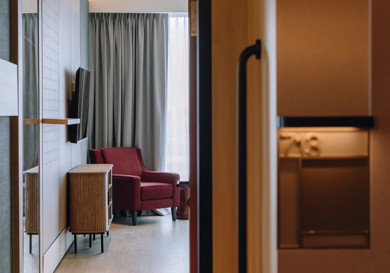 A suite at Care Collective seen from the corridor, with a red armchair by a curtained window and a wall-mounted TV
